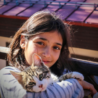 HOME 16 Menina sorridente abraçando um gato filhote malhado em um ambiente ensolarado.