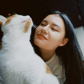 HOME 17 Mulher jovem de cabelos escuros fechando os olhos e encostando o rosto carinhosamente em um gato branco com manchas laranjas