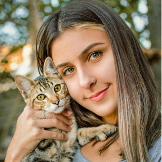 HOME 18 Menina abraçada com gato malhado (tabby) olhando para a câmera em ambiente externo iluminado