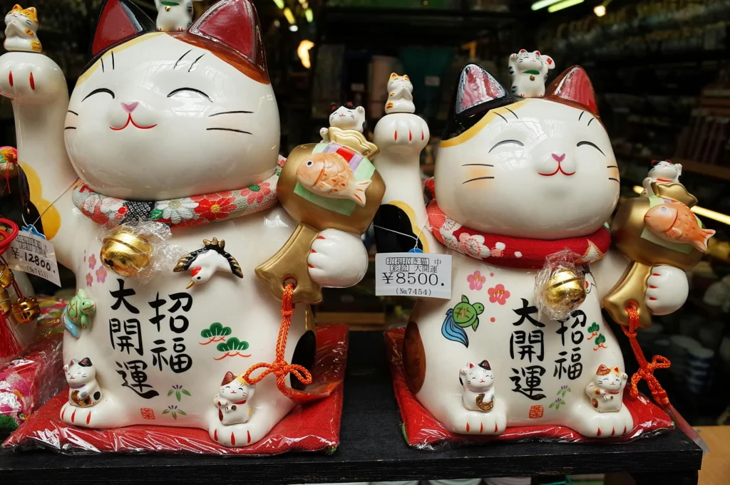 Duas estátuas de cerâmica do maneki-neko, o tradicional gato da sorte japonês com a pata levantada, símbolo de prosperidade e proteção espiritual no Japão.