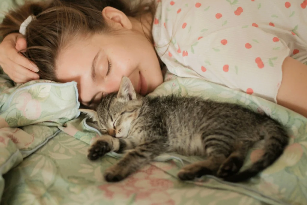 12 Sinais de que Você é um Excelente Tutor e que o Gato Te Escolheu 4 Gatinho filhote dormindo profundamente encostado no rosto da sua tutora na cama, um dos principais sinais de que o gato escolheu seu humano favorito